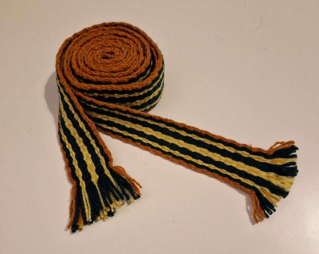 A woven belt is curled up and sitting on a table.